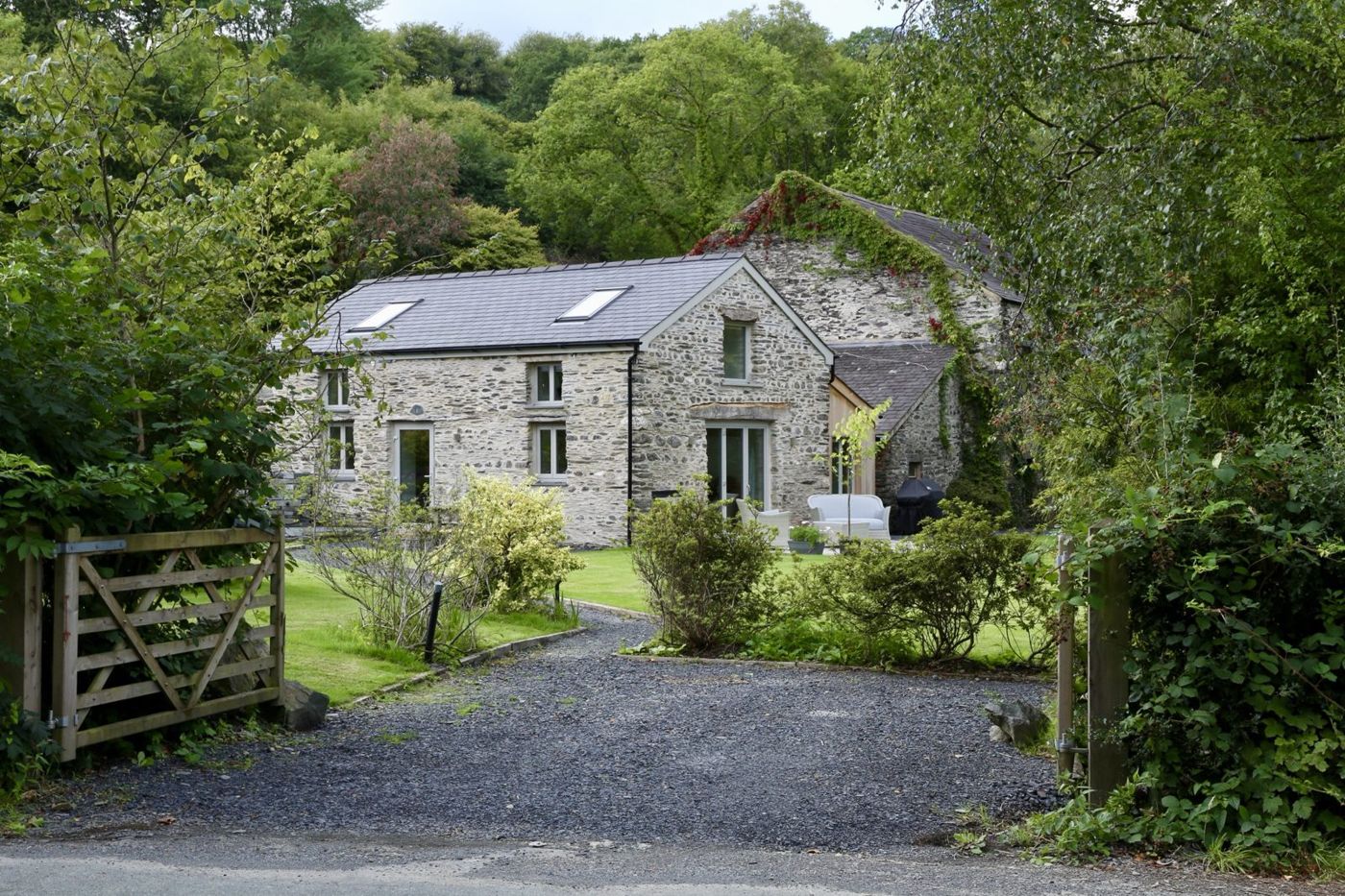 The Cottage from the lane: a stone house with a slate roof behind a wooden gate and gravel drive