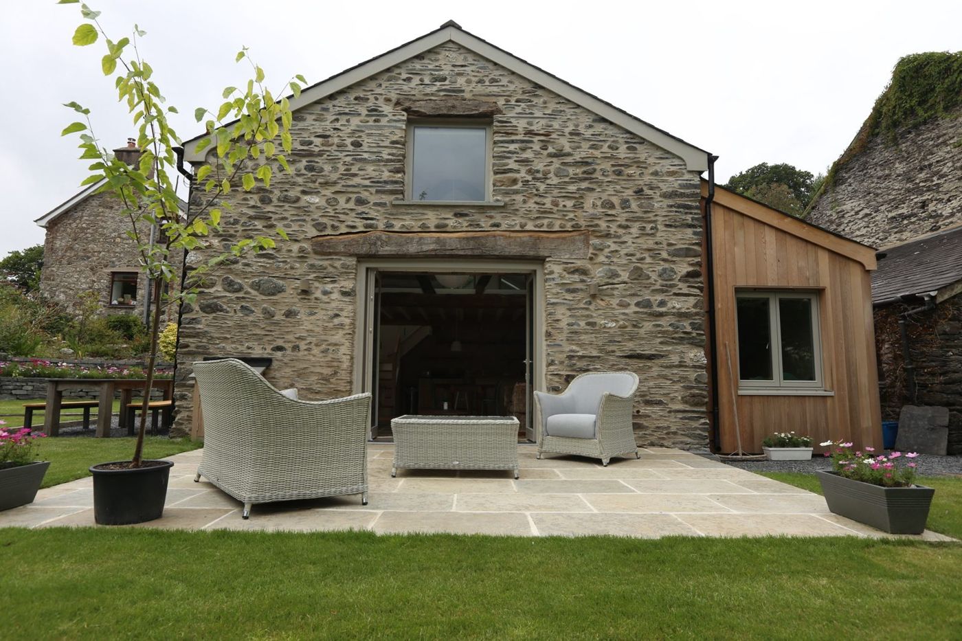 The Cottage’s stone gable and terrace, with two rattan chairs on the flagstones and the lawn beyond