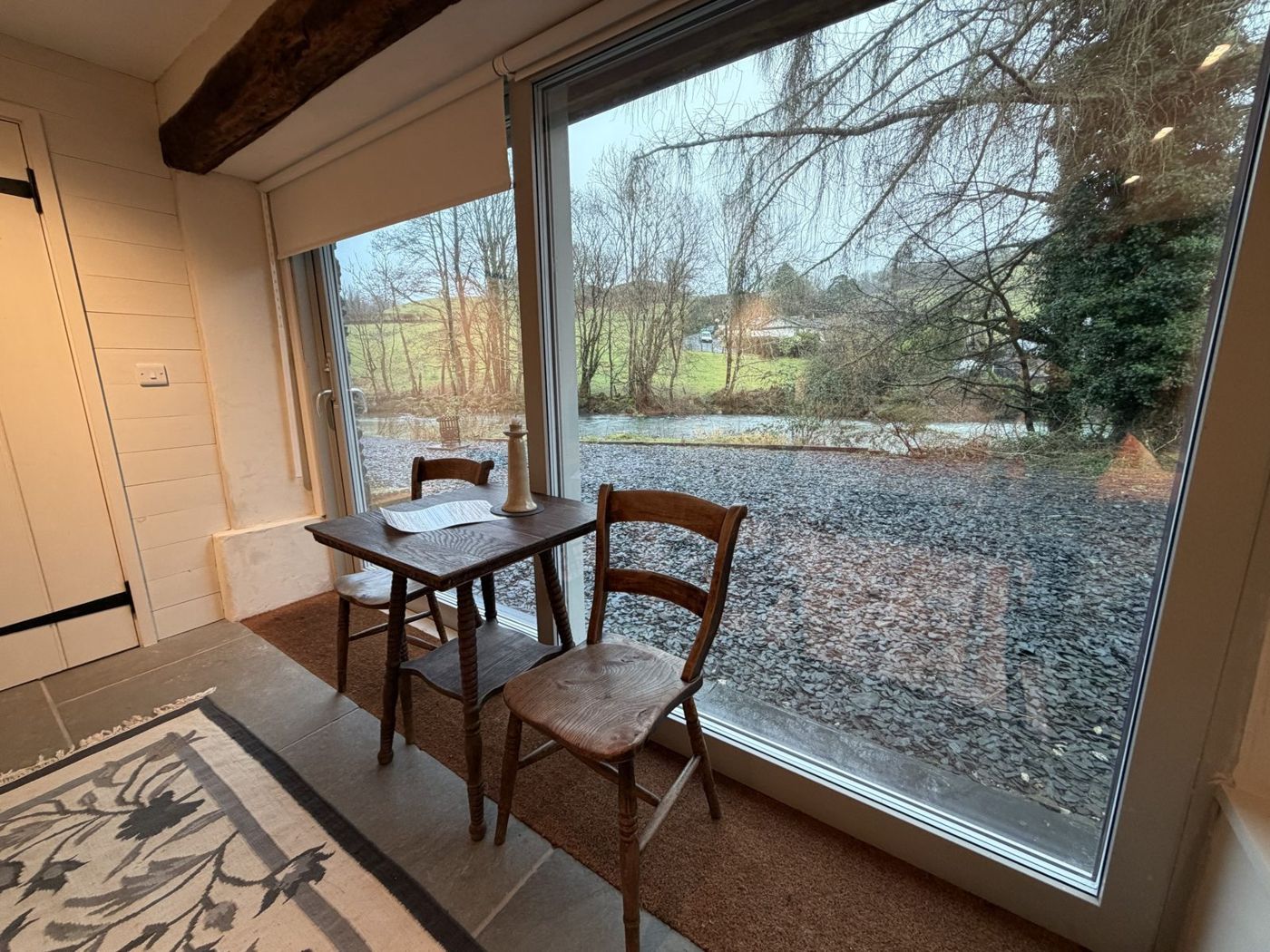 A small wooden table and two chairs by the window, looking out at the river